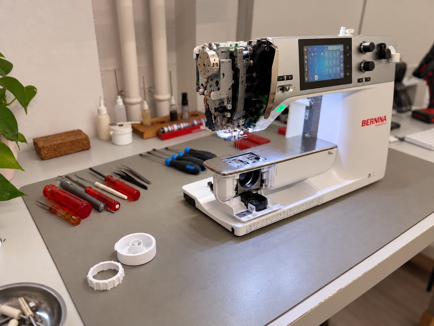 Bernina Computer-Nähmaschine mit abgenommener Kopfverkleidung auf dem aufgeräumten Werkstatttisch, daneben Schraubenzieher, Pinzetten und ausgebaute Teile