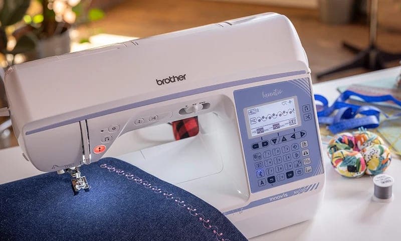 Brother Innov-is NV1350 näht einen Zierstich auf Jeansstoff, daneben Nadelkissen und Massband